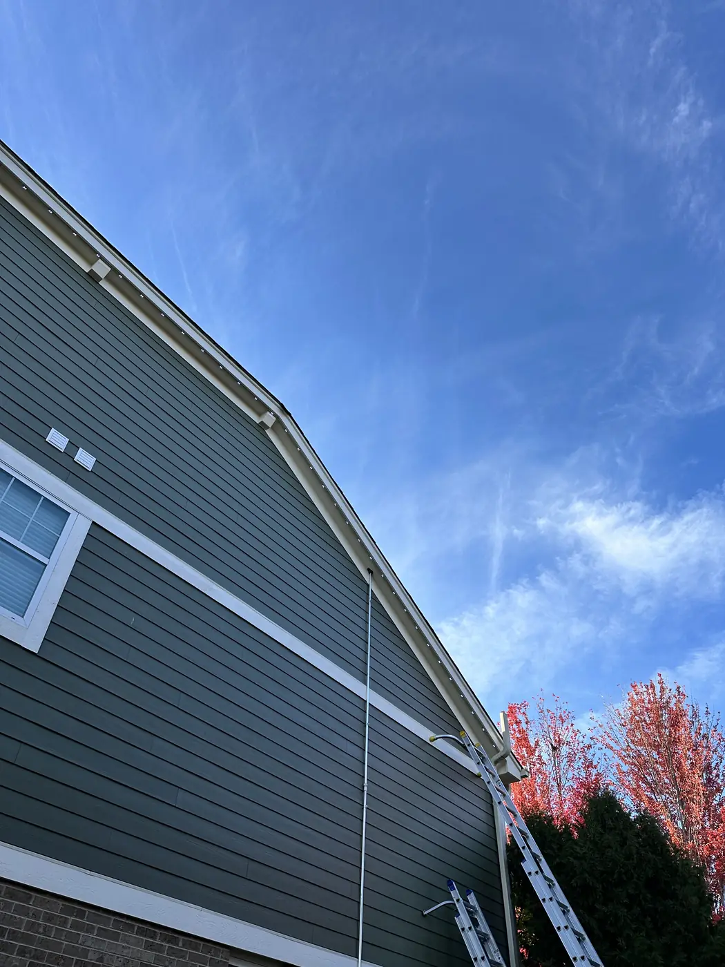 Permanent lighting track in white running along the fascia of a home with dark green siding, nearly indistinguishable from the white trim