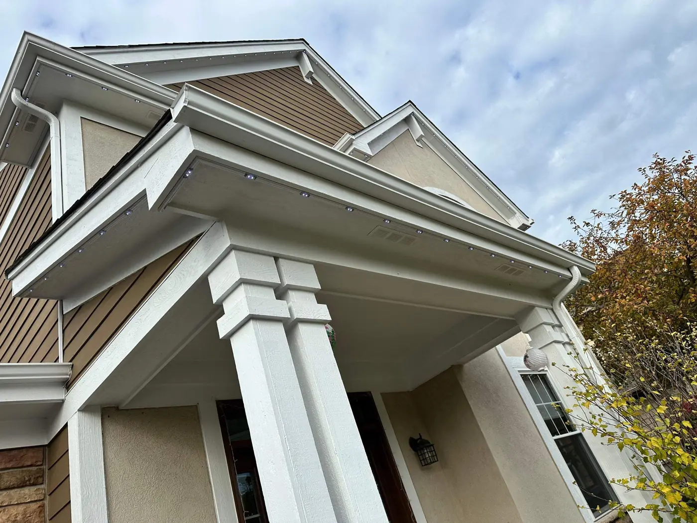 Daytime close view of permanent lighting track mounted under the eave of a Chicagoland home, with small pebble lenses seated in the white channel
