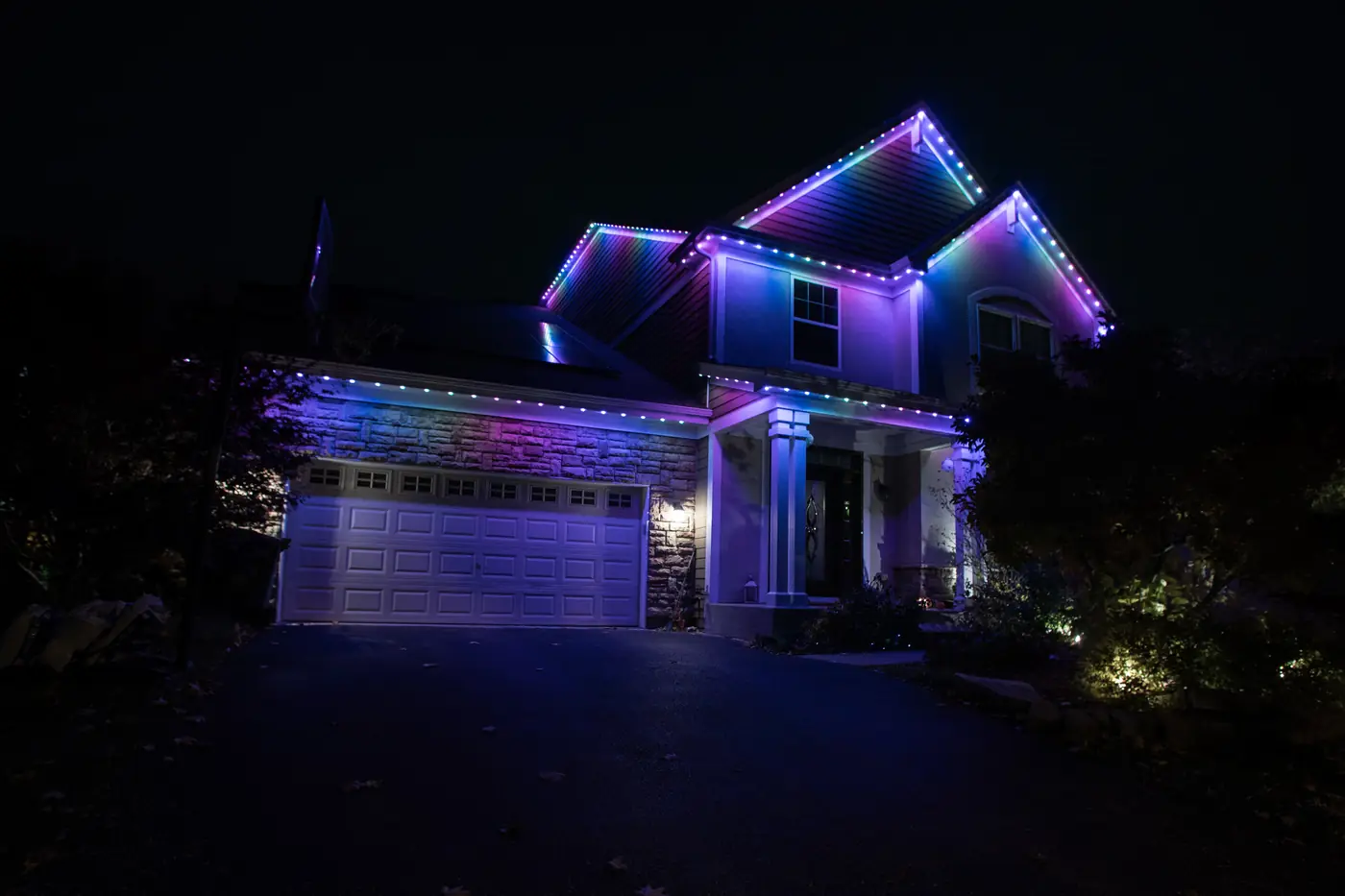 The same Chicagoland home at night with the permanent roofline lighting set to blue and purple